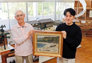 橋本勇次さん（左）から江井の海浜を描いた油絵を受け取る、ｅｉ－ｔｏスタッフの矢野剛史さん＝淡路市江井