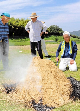わらに粘土をかぶせた窯で土器を焼く「五斗長の風」のメンバーら＝淡路市黒谷