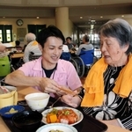 昼食時に入所者の女性に箸を手渡す湯本さん。「男前やし、話も上手。満点や」と女性＝神戸市西区櫨谷町長谷、「大慈弥勒園」