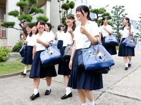 「ＫＯＮＡＮ」の刺しゅうが入ったファミリアのオリジナルかばんを持って歩く甲南女子高校の生徒たち＝神戸市東灘区森北町