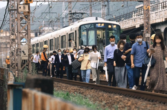 停車した快速電車から降り、線路上を歩いて駅へ向かう乗客ら＝同日午後７時１５分、ＪＲ灘駅近く