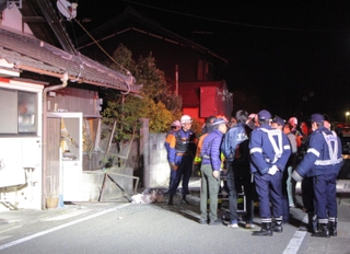 爆発で窓やドアが壊れた民家の前で原因を調べる消防隊員や警察官たち＝12日午後10時３分、丹波市山南町長野