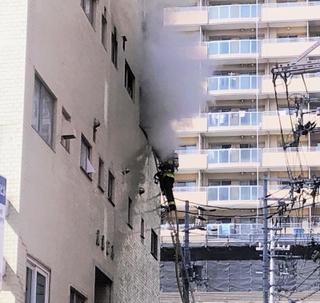 激しく白煙が上がるビルと消火活動をする消防隊員＝11日午後１時５５分、神戸市中央区下山手通３