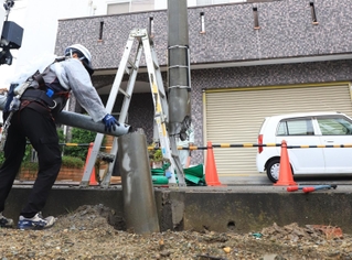 電柱が折れ、応急処置をする作業員＝１８日午前１０時３分、伊丹市東野２