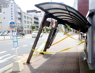 事故の衝撃で、近くのビルに倒れかかるように傾いたバス停の上屋。一時は規制線が張られた＝７日午前、明石市樽屋町