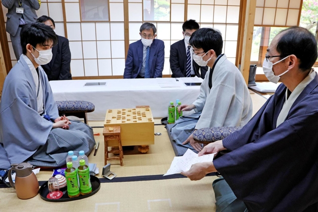 立会人の木村一基九段（右）から封じ手を示される藤井聡太王位（左）。右から２人目は豊島将之九段＝２５日午前、徳島市、渭水苑