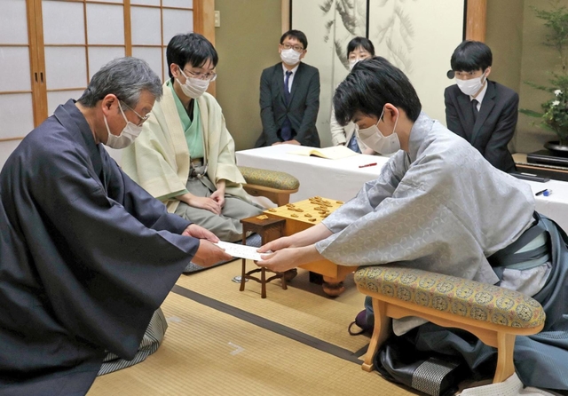 立会人の青野照市九段（左）に封じ手を渡す藤井聡太王位。左から２人目は豊島将之九段＝５日午後、静岡県牧之原市、平田寺