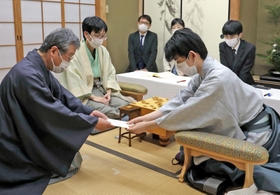 立会人の青野照市九段（左）に封じ手を渡す藤井聡太王位。左から２人目は豊島将之九段＝５日午後、静岡県牧之原市、平田寺
