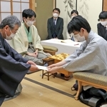 立会人の青野照市九段（左）に封じ手を渡す藤井聡太王位。左から２人目は豊島将之九段＝５日午後、静岡県牧之原市、平田寺