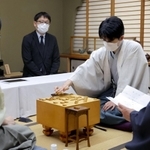 立会人の青野照市九段（右）が封じ手を開封した後、対局を再開する藤井聡太王位（右から２人目）。左は豊島将之九段＝６日午前、静岡県牧之原市、平田寺