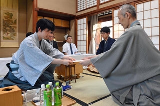 立会人の中田功八段（右）に封じ手を渡す藤井聡太王位（左）。右から２人目は佐々木大地七段＝１５日午後、佐賀県嬉野市、和多屋別荘