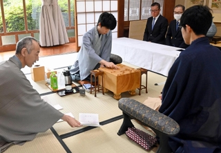 立会人の中田功八段（左）から封じ手を示される佐々木大地七段（右）。中央は着手する藤井聡太王位（中央）＝１６日午前、佐賀県嬉野市、和多屋別荘