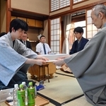 立会人の中田功八段（右）に封じ手を渡す藤井聡太王位（左）。右から２人目は佐々木大地七段＝１５日午後、佐賀県嬉野市、和多屋別荘