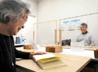 音訳ボランティアによる対面朗読を聞く松森斉さん（右）。好きな中国の歴史小説は漢字が多く、読み上げ機能では誤読が多いという＝明石市大明石町１、あかし市民図書館