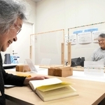 音訳ボランティアによる対面朗読を聞く松森斉さん（右）。好きな中国の歴史小説は漢字が多く、読み上げ機能では誤読が多いという＝明石市大明石町１、あかし市民図書館
