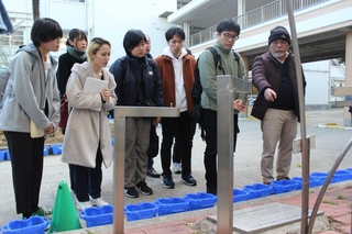 慰霊モニュメントの前で、松田満さん（右から１人目）から震災で亡くなった児童の話を聞く自由人会の杉野じんべえ（同２人目）ら＝西宮市樋ノ口町２、樋ノ口小