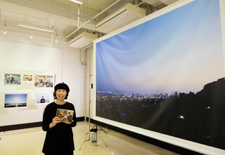 写真家の平野愛さん。六甲山から撮った薄暮の神戸の街並みの前で＝神戸市中央区小野浜町１、デザイン・クリエイティブセンター神戸