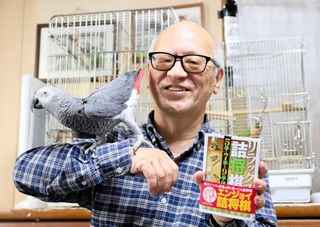 新著を手にする森信雄七段。詰め将棋を作っていると、駒を動かしてしまうヨウムの金太郎（左）＝宝塚市内