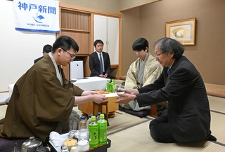 立会人の福崎文吾九段（右端）に封じ手を渡す永瀬拓矢九段（左）。右から２人目は藤井聡太王位＝１５日午後、神戸市北区有馬町、中の坊瑞苑（撮影・風斗雅博）