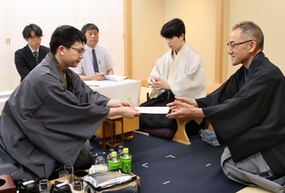 立会人の島朗九段（右）に封じ手を渡す永瀬拓矢九段（左）。中央は藤井聡太王位＝29日午後、北海道千歳市、ポルトムインターナショナル北海道