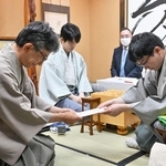 立会人の佐藤康光九段（左）に封じ手を渡す永瀬拓矢九段（右）。左から２人目は藤井聡太王位＝５日午後、愛知県小牧市、合掌レストラン大蔵