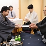 立会人の島朗九段（右）に封じ手を渡す永瀬拓矢九段（左）。中央は藤井聡太王位＝29日午後、北海道千歳市、ポルトムインターナショナル北海道