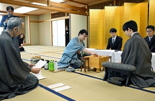 立会人の中田功八段（左）から封じ手を示された後、着手する永瀬拓矢九段（中央）。手前右は藤井聡太王位＝２０日午前、福岡県宗像市、宗像ユリックス
