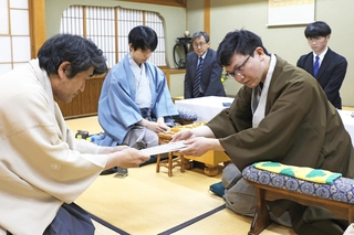 立会人の森内俊之九段（左）に封じ手を渡す永瀬拓矢九段（手前右）。左から２人目は藤井聡太王位＝２６日午後、徳島市、渭水苑