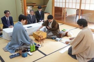 立会人の森内俊之九段（右）から封じ手を示された後、着手する永瀬拓矢九段（右から２人目）。手前左は藤井聡太王位＝27日午前、徳島市、渭水苑