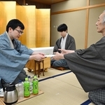 立会人の中田功八段（右）に封じ手を渡す永瀬拓矢九段（手前左）。中央は藤井聡太王位＝１９日午後、福岡県宗像市、宗像ユリックス