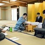 立会人の中田功八段（左）から封じ手を示された後、着手する永瀬拓矢九段（中央）。手前右は藤井聡太王位＝２０日午前、福岡県宗像市、宗像ユリックス