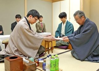 立会人の青野照市九段（右）に封じ手を渡す永瀬拓矢九段（手前左）。右から２人目は藤井聡太王位＝９日午後、東京都渋谷区、将棋会館