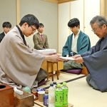 立会人の青野照市九段（右）に封じ手を渡す永瀬拓矢九段（手前左）。右から２人目は藤井聡太王位＝９日午後、東京都渋谷区、将棋会館