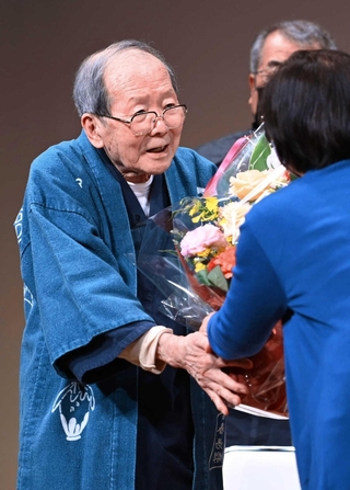 「一人語り劇場」最後の舞台を終え、関係者らから花束を受け取る上方芸能評論家の木津川計さん＝２０２２年４月１０日午後、神戸市灘区岸地通１、灘区民ホール