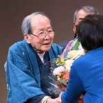 「一人語り劇場」最後の舞台を終え、関係者らから花束を受け取る上方芸能評論家の木津川計さん＝２０２２年４月１０日午後、神戸市灘区岸地通１、灘区民ホール