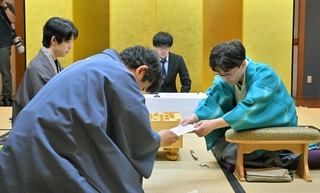 立会人の森内俊之九段（手前）に封じ手を手渡す伊藤匠二冠（右）。左は藤井聡太王位＝４日午後、浜松市、浜松八幡宮楠俱楽部