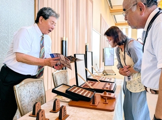 王位戦前夜祭に展示されたオールレザーの将棋盤と駒について説明する服部清隆さん（左）＝有馬グランドホテル
