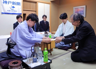 立会人の福崎文吾九段（右）に封じ手を渡す伊藤匠二冠。右から２人目は藤井聡太王位＝１５日午後、神戸市北区有馬町、中の坊瑞苑（撮影・吉田敦史）