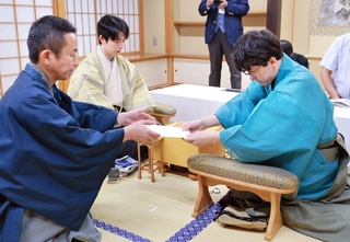 立会人の屋敷伸之九段（左）に封じ手を渡す伊藤匠二冠（右）。中央は藤井聡太王位＝29日午後、北海道登別市、祝いの宿　登別グランドホテル