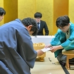 立会人の森内俊之九段（手前）に封じ手を手渡す伊藤匠二冠（右）。左は藤井聡太王位＝４日午後、浜松市、浜松八幡宮楠俱楽部