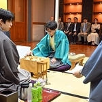 立会人の森内俊之九段（右）から封じ手を示された藤井聡太王位（手前左）。中央は伊藤匠二冠＝５日午前、浜松市、浜松八幡宮楠俱楽部