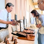 王位戦前夜祭に展示されたオールレザーの将棋盤と駒について説明する服部清隆さん（左）＝有馬グランドホテル