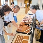 王位戦前夜祭に展示された牛革製の将棋盤と駒について説明する服部清隆さん（右）＝有馬グランドホテル