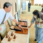 王位戦前夜祭に展示された牛革製の将棋盤と駒について説明する服部清隆さん（左）＝有馬グランドホテル