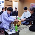 立会人の福崎文吾九段（右）に封じ手を渡す伊藤匠二冠。右から２人目は藤井聡太王位＝１５日午後、神戸市北区有馬町、中の坊瑞苑（撮影・吉田敦史）