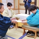 立会人の屋敷伸之九段（左）に封じ手を渡す伊藤匠二冠（右）。中央は藤井聡太王位＝29日午後、北海道登別市、祝いの宿　登別グランドホテル
