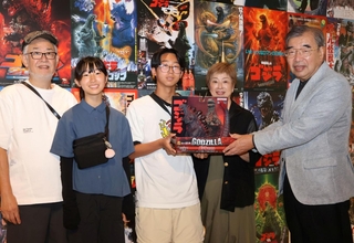 歴代の映画ポスターの前で岡泰正会長（右端）から記念品を受け取った井筒風太さん（中央）と家族＝神戸市東灘区向洋町中２、神戸ゆかりの美術館