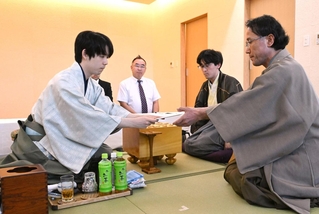 立会人の深浦康市九段（右）に封じ手を渡す藤井聡太王位（左）。右から２人目は伊藤匠二冠＝１８日午後、長崎市、ガーデンテラス長崎ホテル＆リゾート