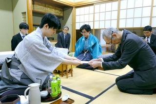 立会人の中田功八段（手前右）に封じ手を渡す藤井聡太王位（手前左）。中央奥は伊藤匠二冠＝２６日午後、徳島市、渭水苑