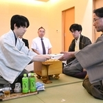 立会人の深浦康市九段（右）に封じ手を渡す藤井聡太王位（左）。右から２人目は伊藤匠二冠＝１８日午後、長崎市、ガーデンテラス長崎ホテル＆リゾート
